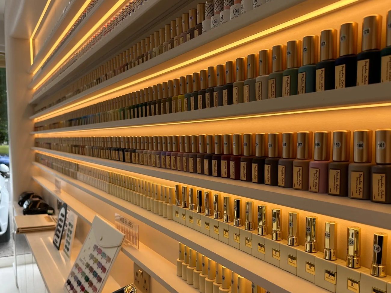 Backlit shelving holding rows of polish bottles along the salon wall